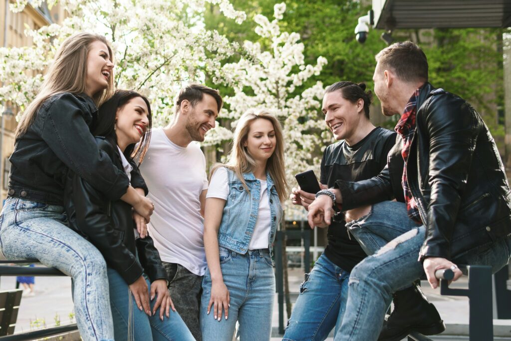A group of trendy millennials sit on benches in a sunny park, for “What are the Best Investments for Millenials?”