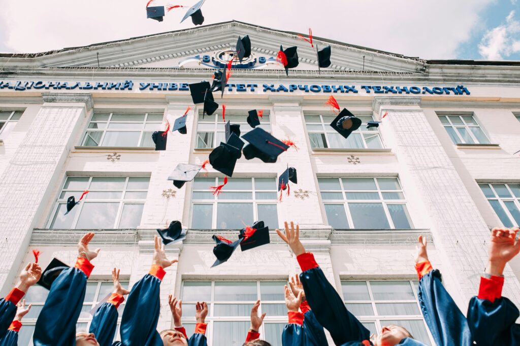 Exterior, graduating students throwing their mortarboard hats into the air, for “A Beginner’s Guide to Alternative Assets: How to Start Investing After College”
